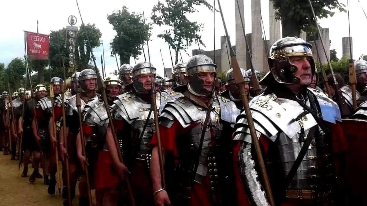 Römische Legionäre in silbernen Rüstungen marschieren in enger Formation mit Helmen und Speeren.