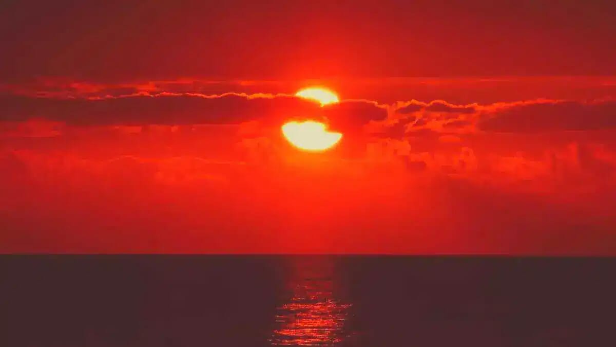 Über dem Meer glüht die Sonne tiefrot am Horizont, während Wolken und Spiegelungen den Abend an der Adria in warmes Licht tauchen.
