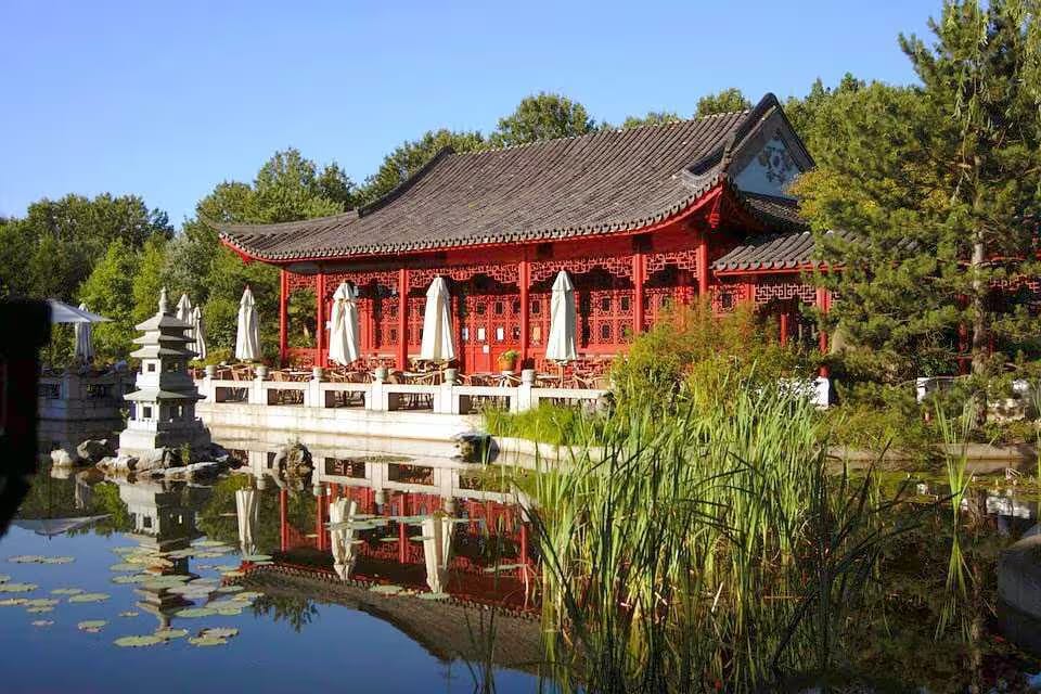 Asiatisches Gebäude mit roten Wänden und Dach, umgeben von Wasser und Pflanzen am Teich.