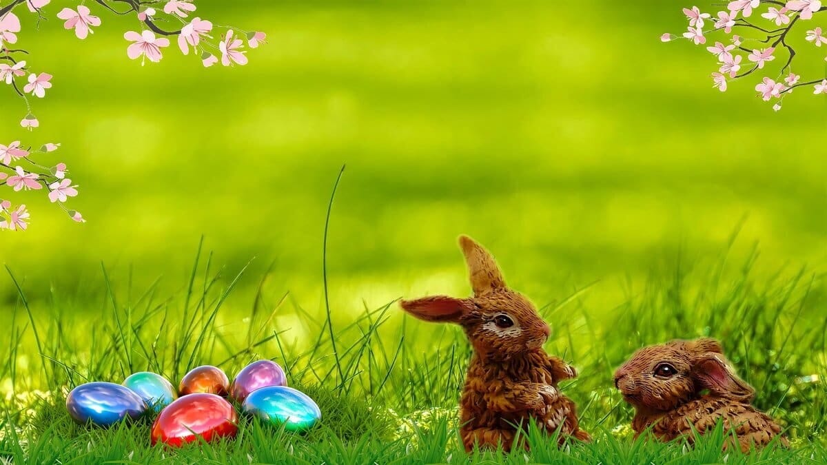 Frohe Ostern, Osterfest, bunte Eier im grünen Gras mit rosa Blüten und Osterhase