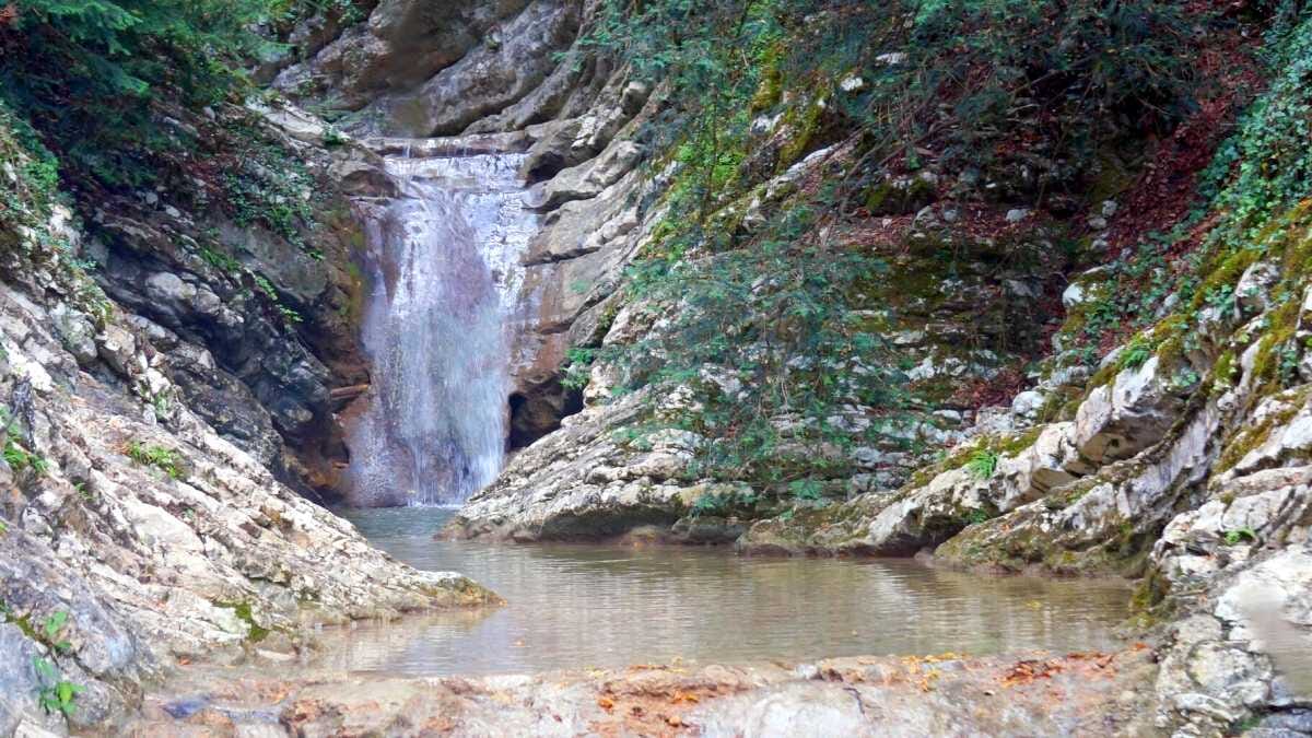 naturlicher Wasserfall in einer Schlucht, umgeben von Felsen und grüner Vegetation, ideal für Naturliebhaber und Wanderer